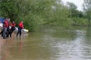 picture of owner and black newfoundland dog on the shore whilst the object is thrown