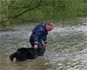 picture of owner and black newfoundland dog entering water at the start of controlled swim