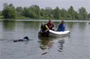 picture of black newfoundland dog approaching a boat with a rope in its mouth